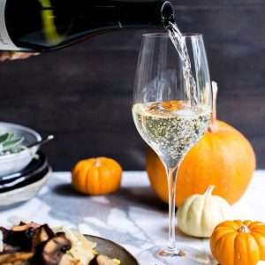 Pouring Chardonnay wine around pumpkins and risotto
