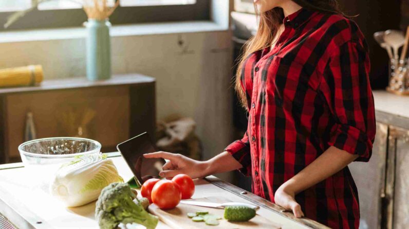 graphicstock cropped image of woman in red shirt standing in kitchen with tablet computer and looking recipes side view BLIeriD7Ohl 1 scaled 1